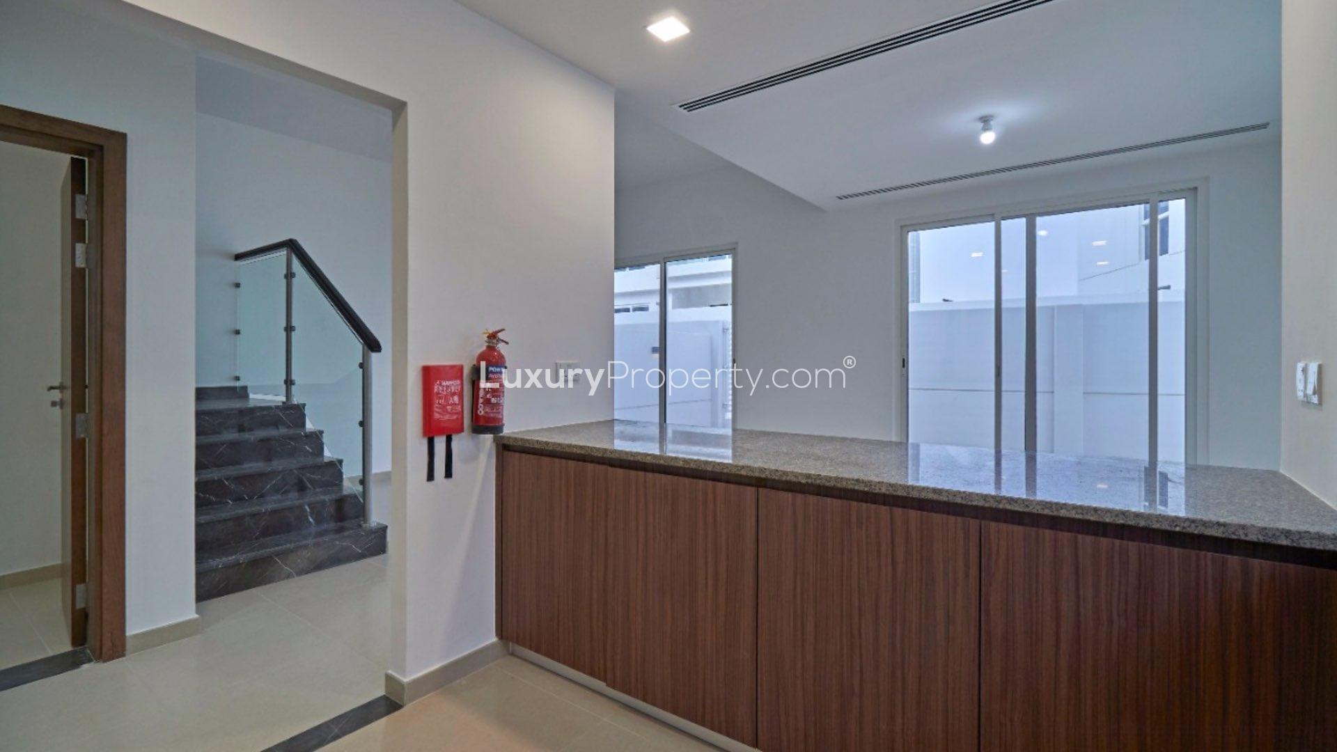 Modern kitchen in 4-bedroom villa, Arabella Townhouses, Mudon, featuring wood cabinets and mosaic backsplash