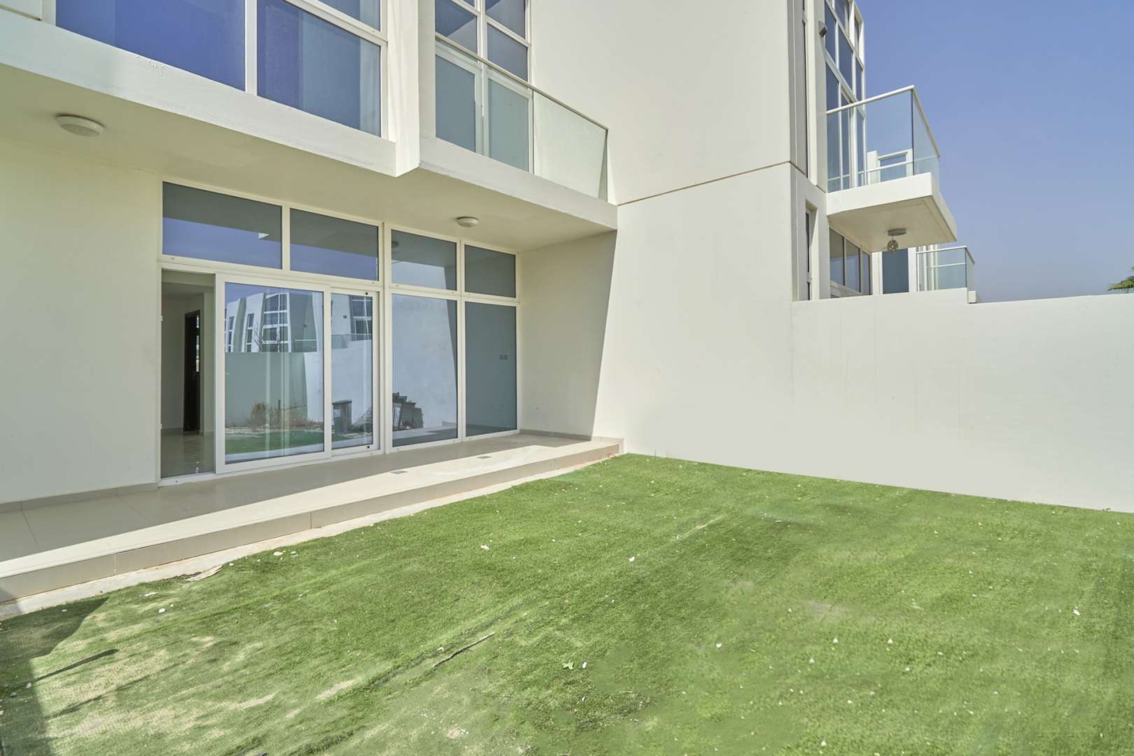 Luxurious villa exterior with glass doors and artificial lawn in Damac Hills 2, Akoya