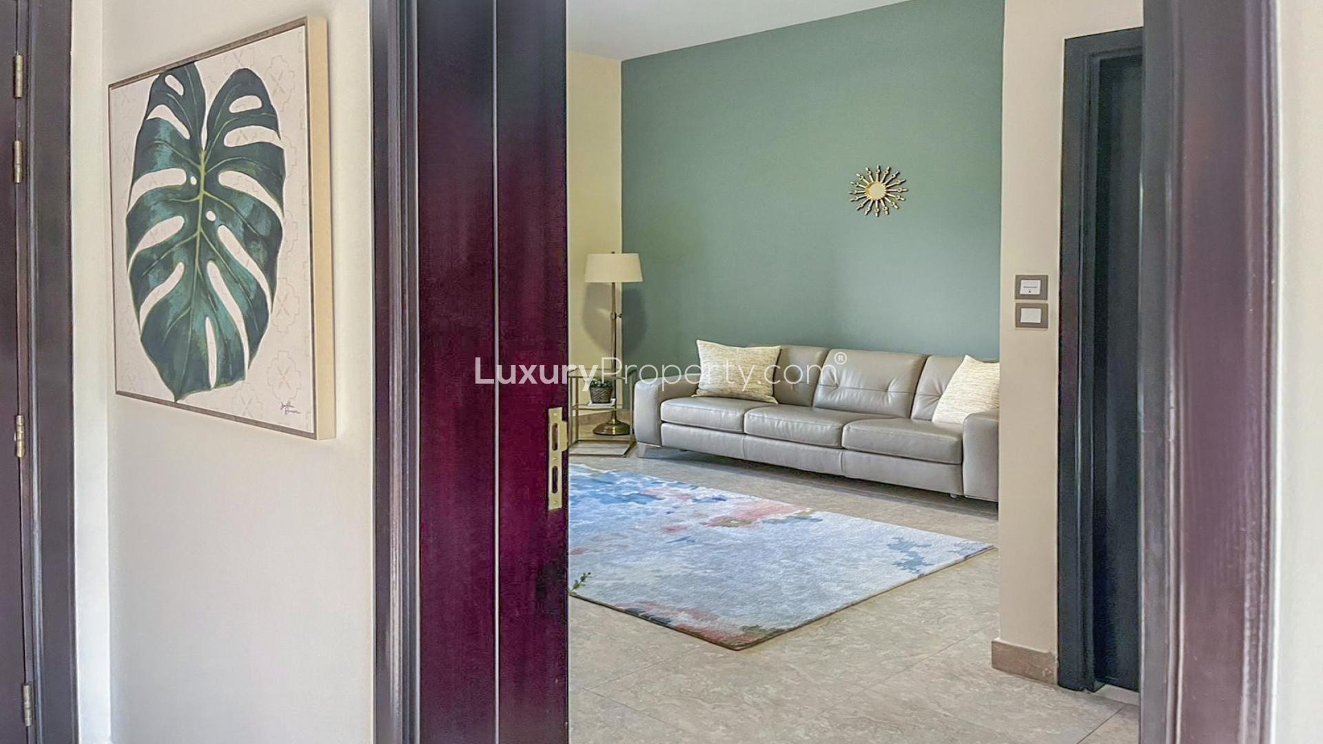 Alt text: "Elegant living room with gray sofa in Mudon townhouse, Naseem community, for sale.",Upgraded townhouse garden with lush greenery in Naseem, Mudon community, available for sale