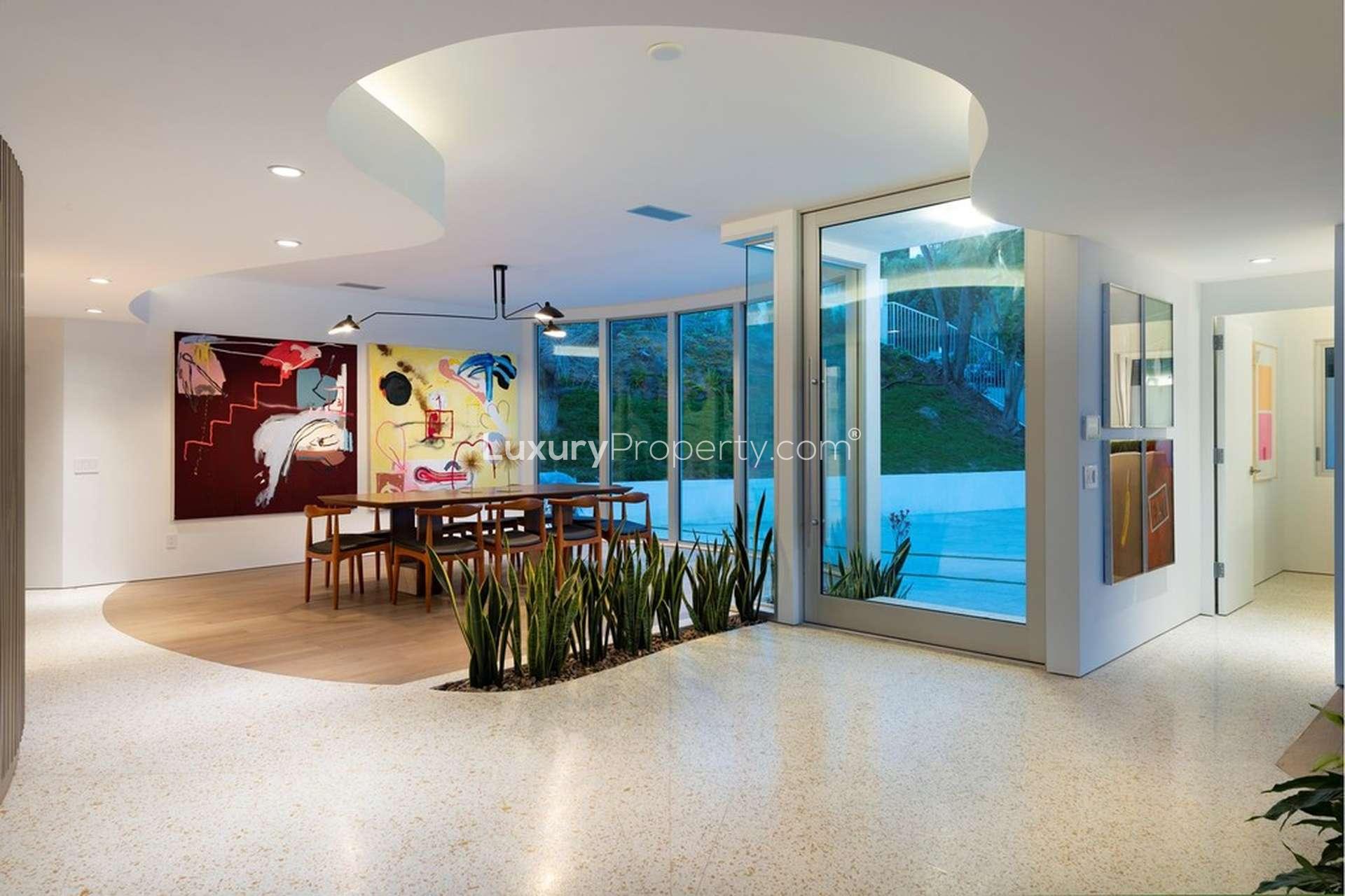 Modern villa exterior with large glass windows, lush lawn, and pool at Rising Glen Rd