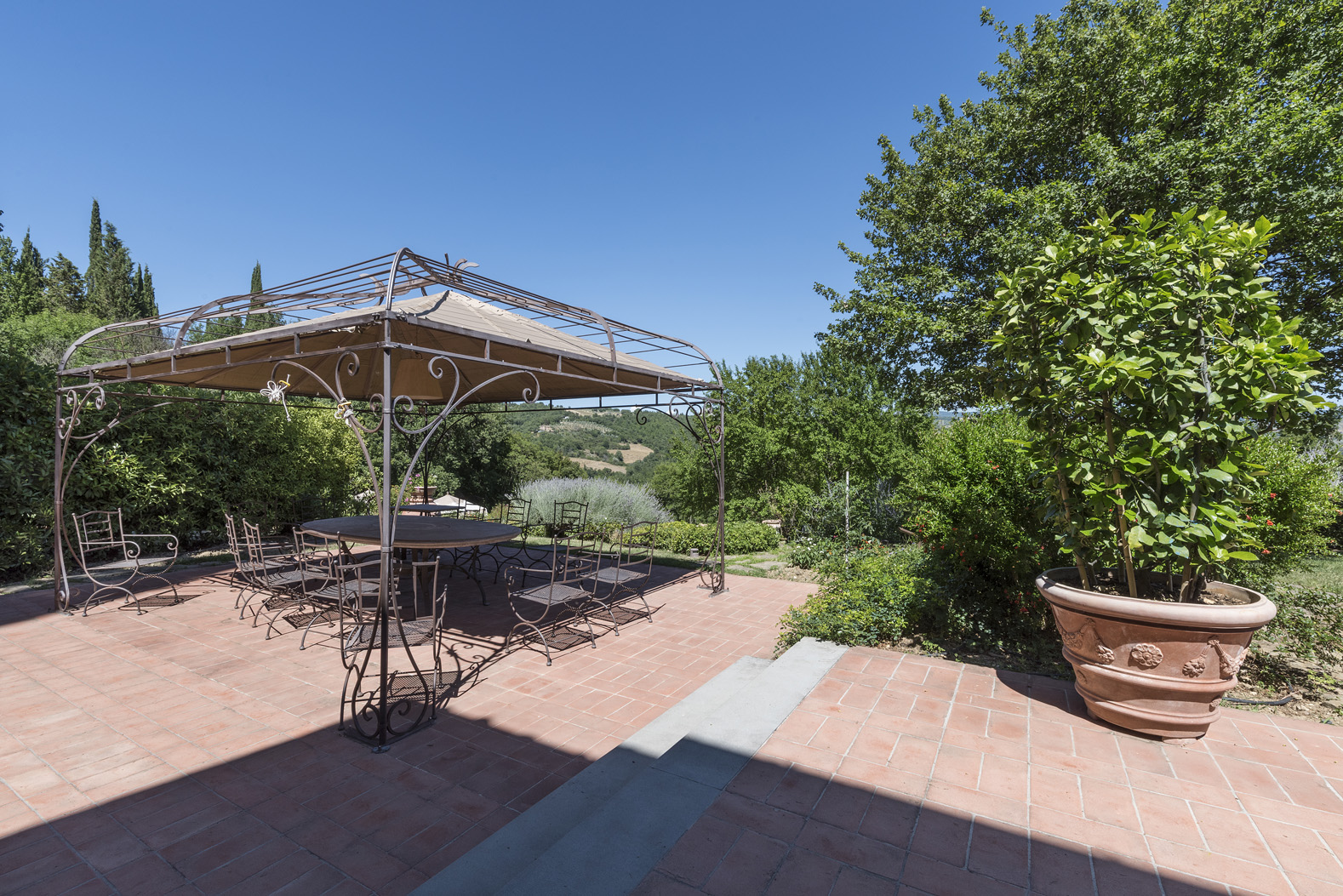 "Stunning villa poolside view in Chianti, Tuscany, surrounded by lush greenery and deck.",Outdoor patio with pergola and garden view at Tuscan villa in Chianti, Florence