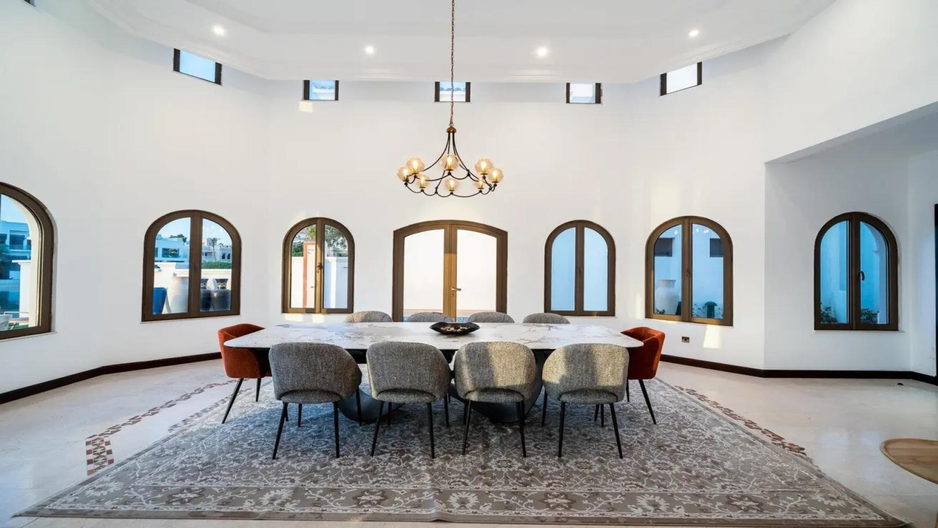 Luxurious dining area in Palm Jumeirah villa with pool view, arched windows, elegant chandelier