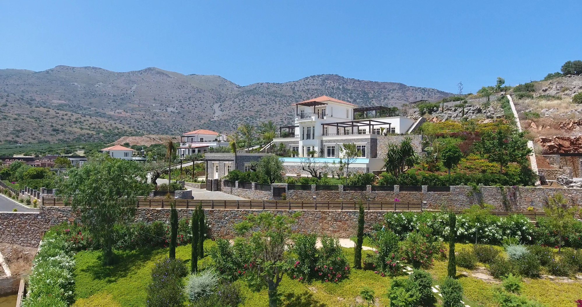 Four-bedroom waterfront villa with lush garden, pool, and stone walls in Crete, Greece