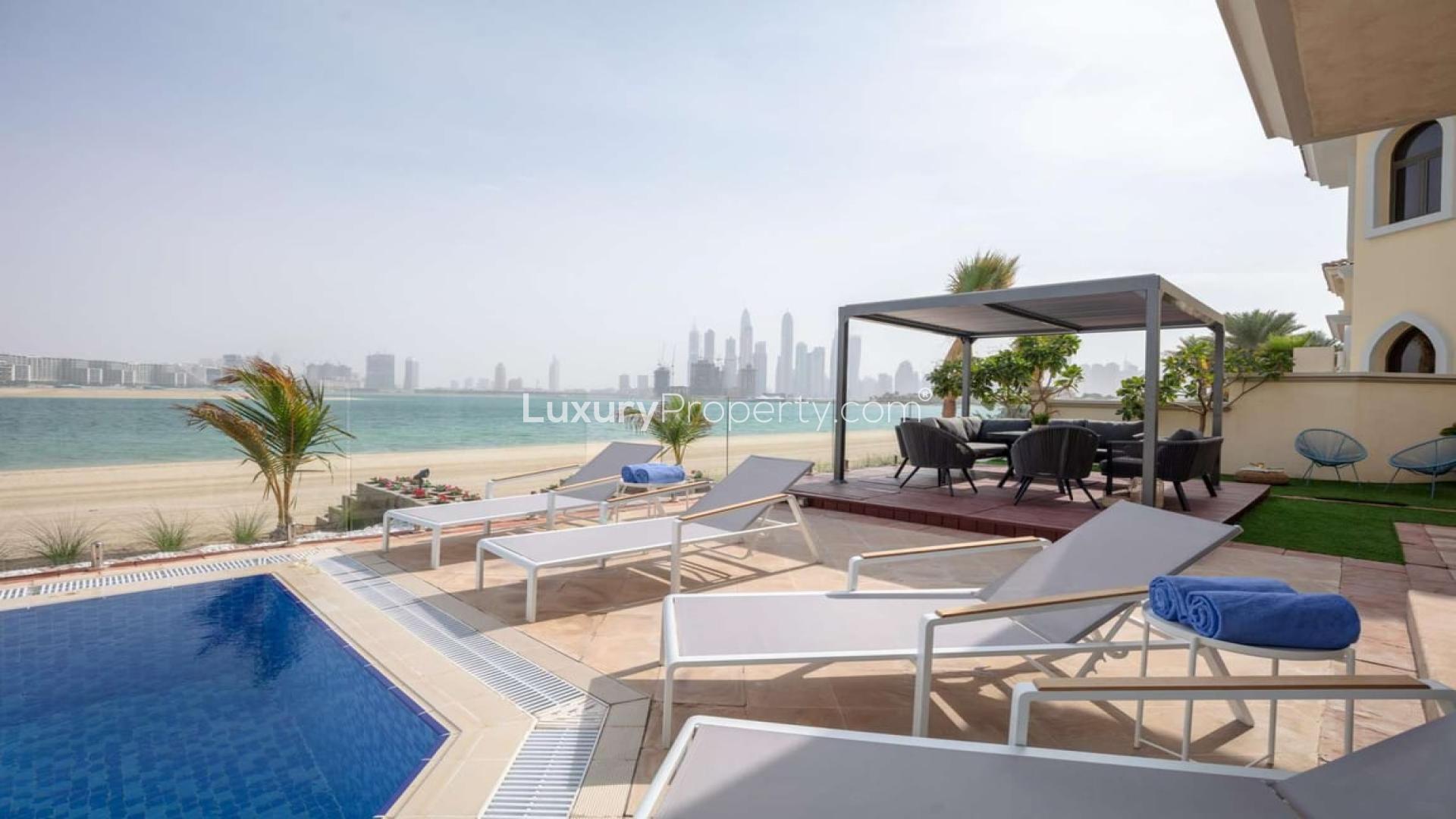 "Luxury villa poolside view at Garden Homes, Palm Jumeirah, available for short-term rental.",Luxurious Palm Jumeirah villa with beachfront view, pool, and outdoor seating area for rent