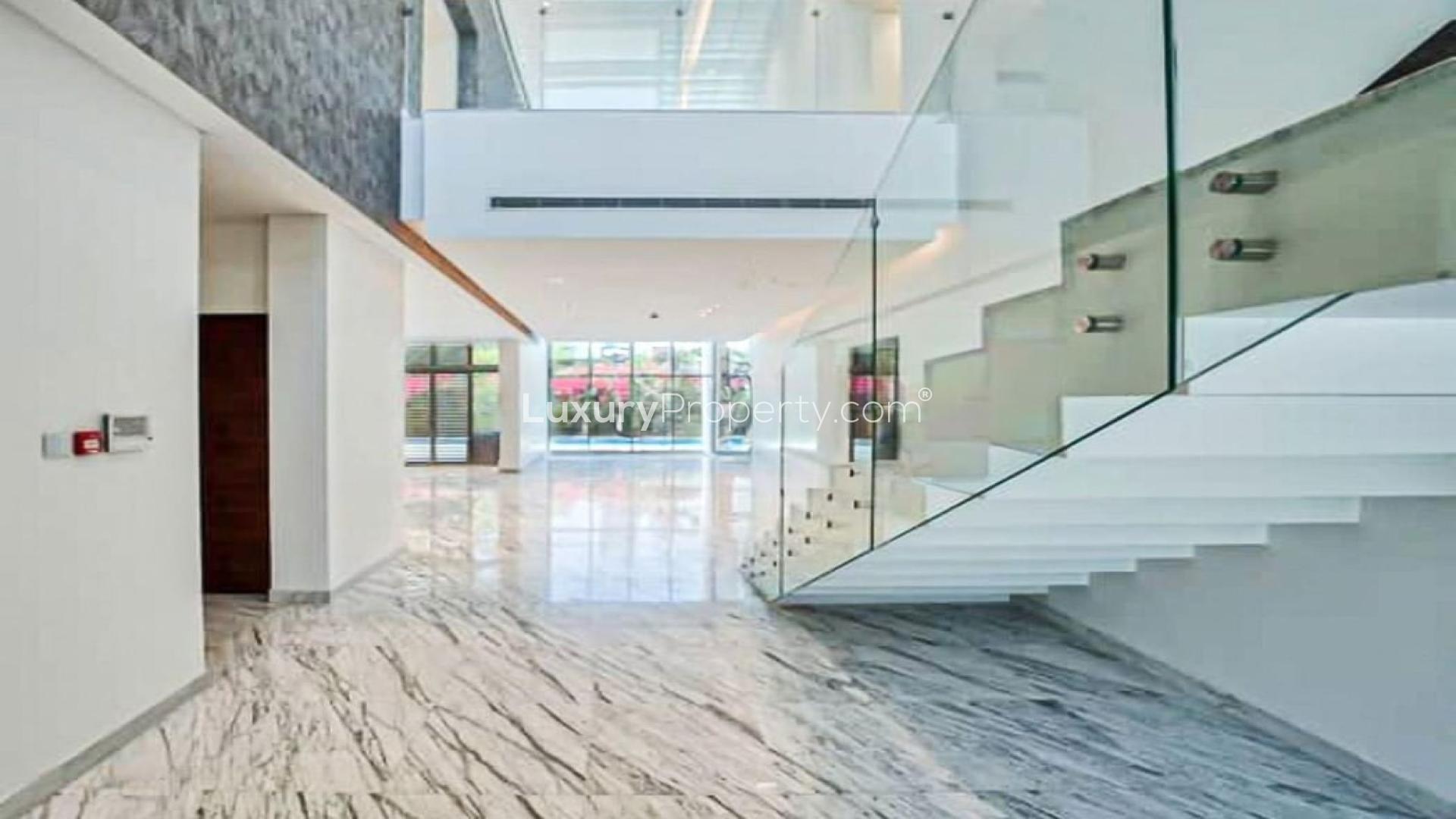 "Spacious living area with marble floors and garden view in District One villa.",Bright, spacious interior of District One villa with modern staircase and marble flooring