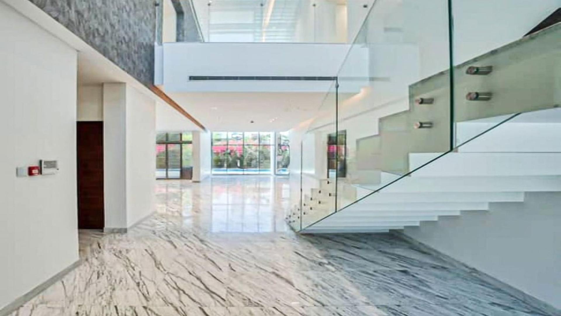 "Spacious living area with marble floors and garden view in District One villa.",Bright, spacious interior of District One villa with modern staircase and marble flooring