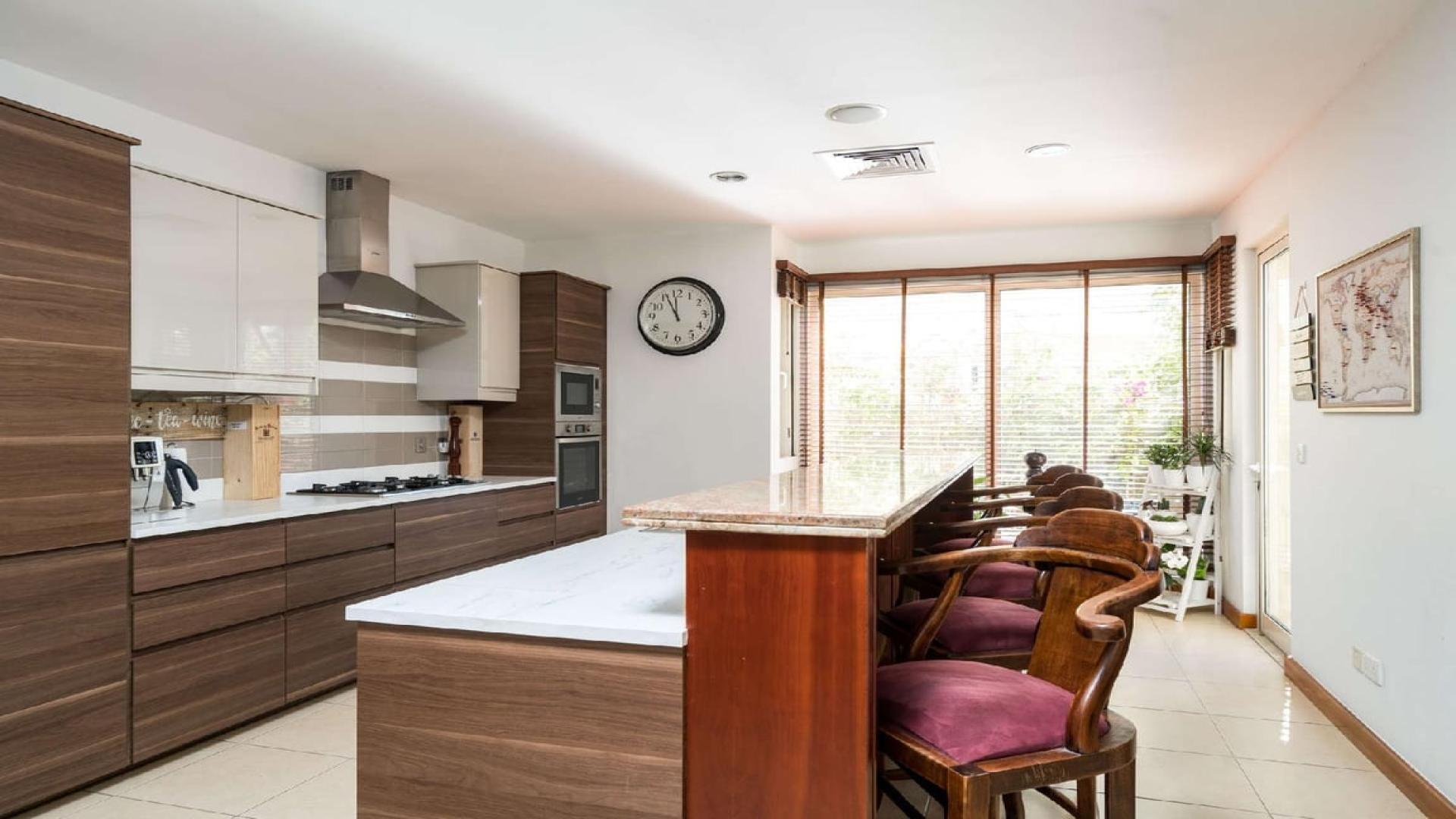 "Elegant villa interior with modern staircase, Arabian Ranches, Savannah community, for sale.",Modern kitchen with wooden cabinetry and breakfast bar in Savannah villa, Arabian Ranches