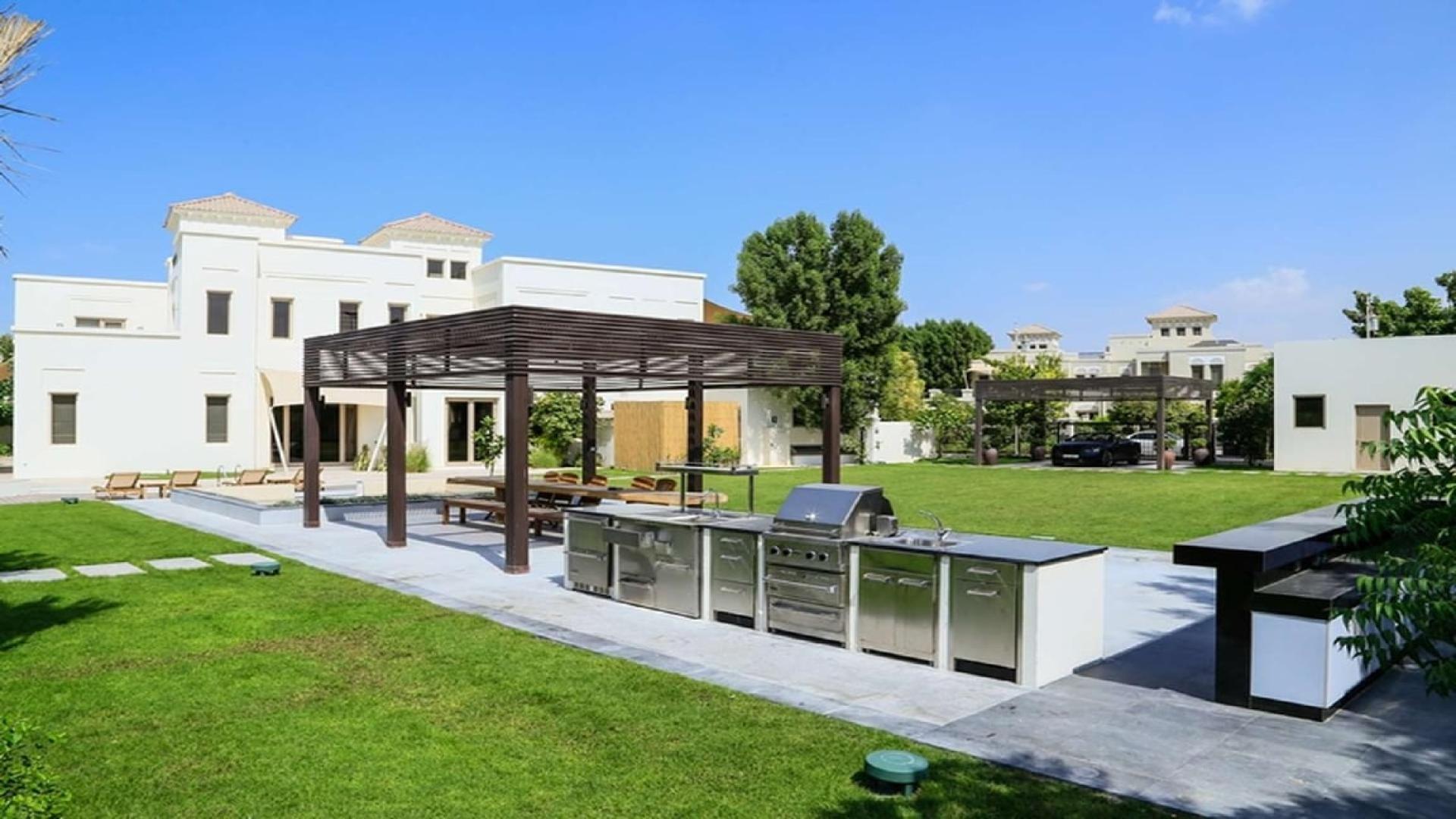 Lush villa garden with pool and pergola overlooking lake in Ajman Uptown