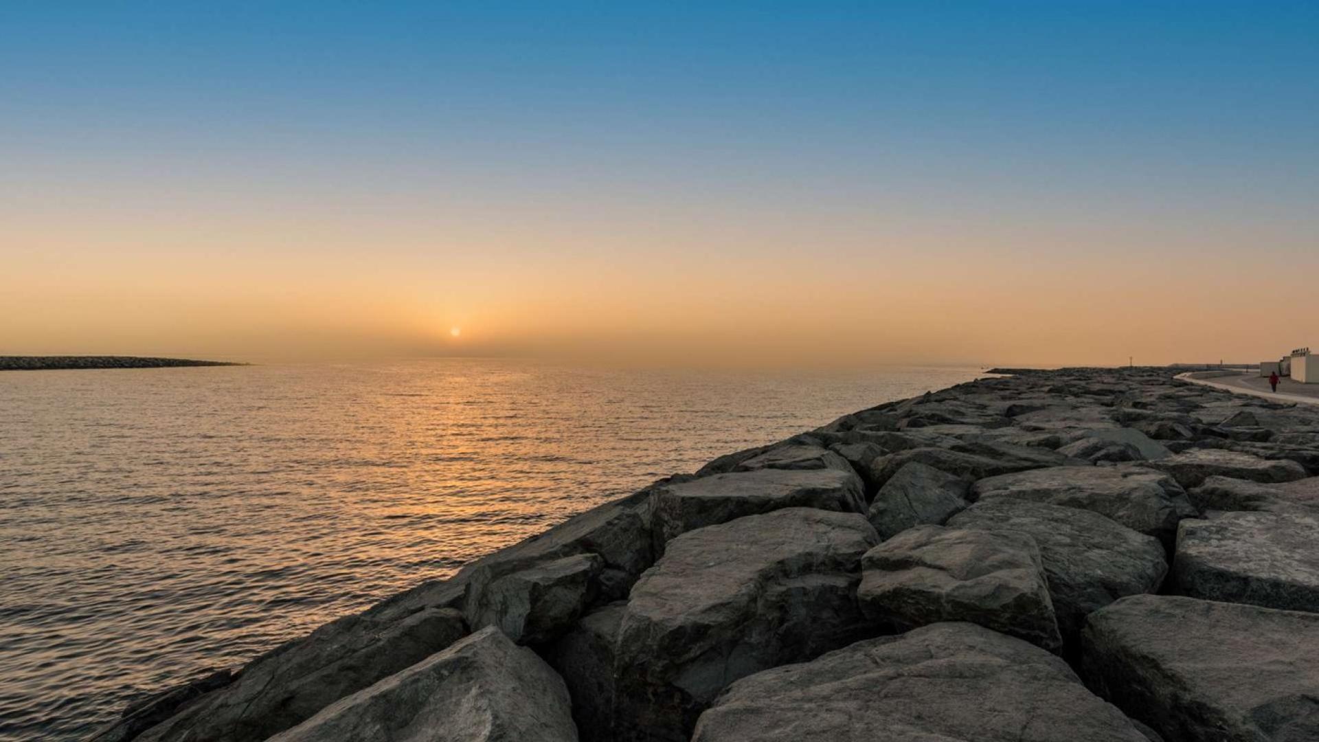 Sunset view from Pearl Jumeirah waterfront, showcasing serene sea and rocky shoreline