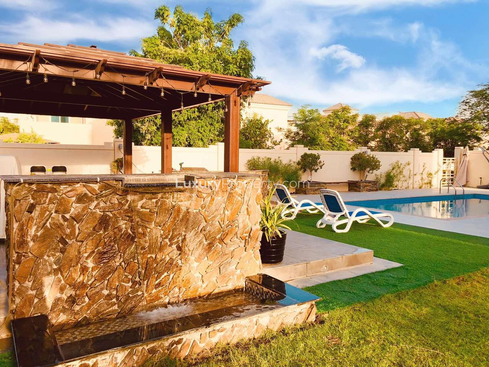 "Spacious white built-in wardrobes in 5-bedroom C2 villa, Victory Heights, Dubai Sports City.",Luxurious villa in Victory Heights with pool, stone waterfall, and outdoor seating area