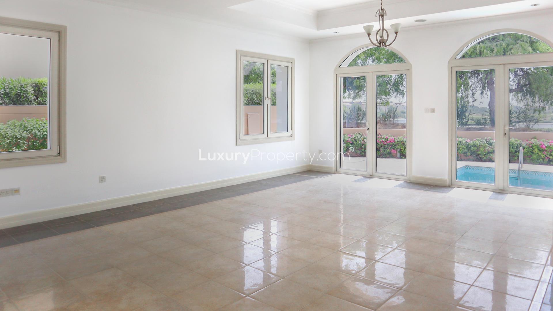 "Elegant villa exterior in Jumeirah Golf Estates, Fire community, with garage and lush landscaping.",Bright villa interior with large windows overlooking garden and pool in Jumeirah Golf Estates