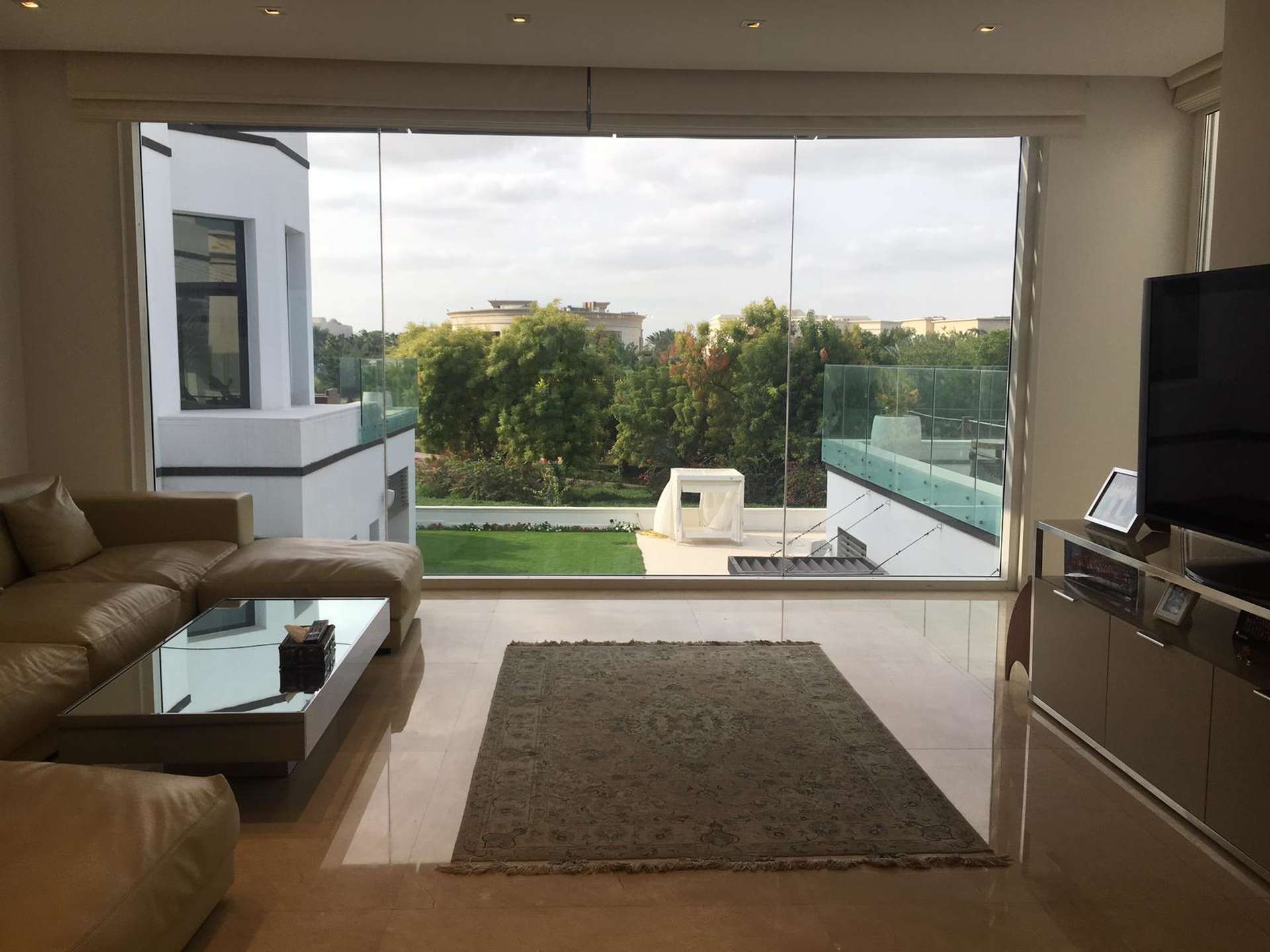 "Modern 5-bedroom villa exterior with pool, blue lighting, Emirates Hills, for rent.",Contemporary living room with large windows in Emirates Hills villa for rent, Sector R