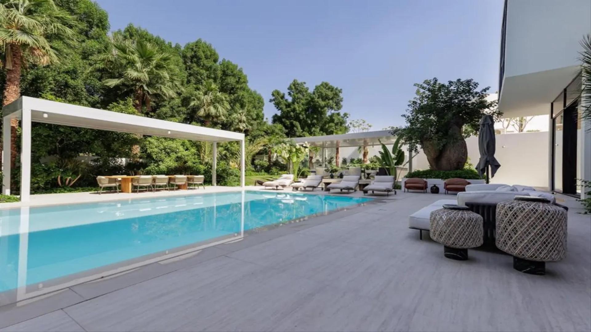 "Spacious luxury living room in Al Barari mansion villa with modern decor and high ceilings.",Luxurious Al Barari mansion villa poolside view with modern outdoor seating, The Nest community