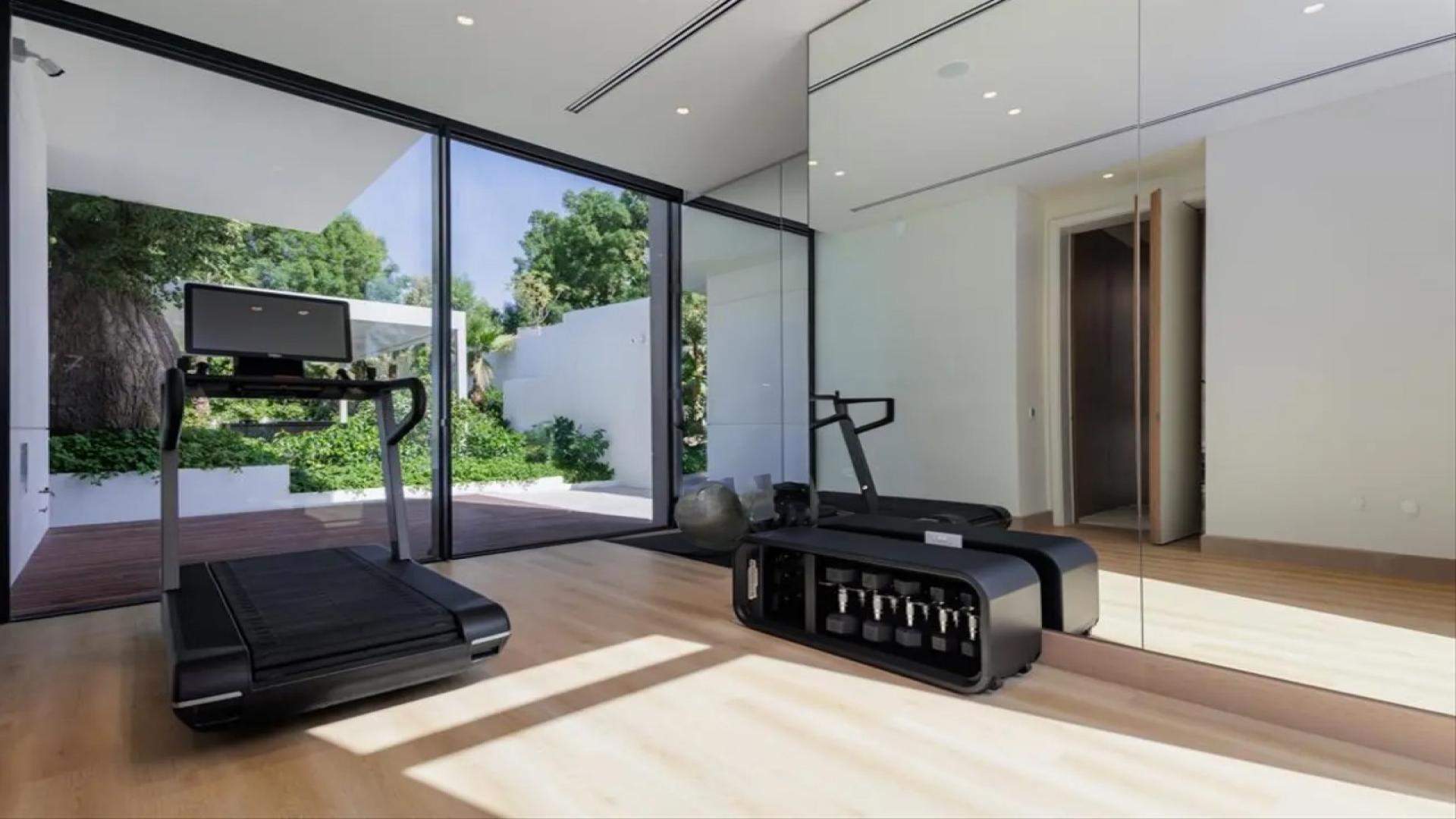 Luxury home gym in Al Barari villa with treadmill and weights, glass wall view