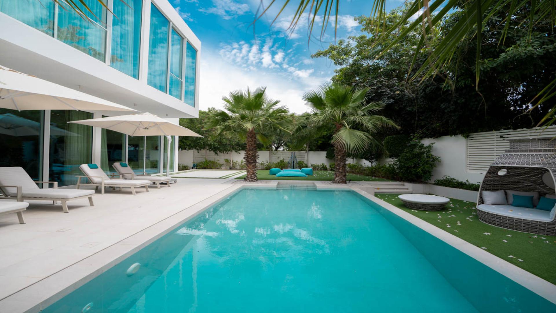 Luxury villa in Al Barari with poolside view, palm trees, and modern outdoor seating