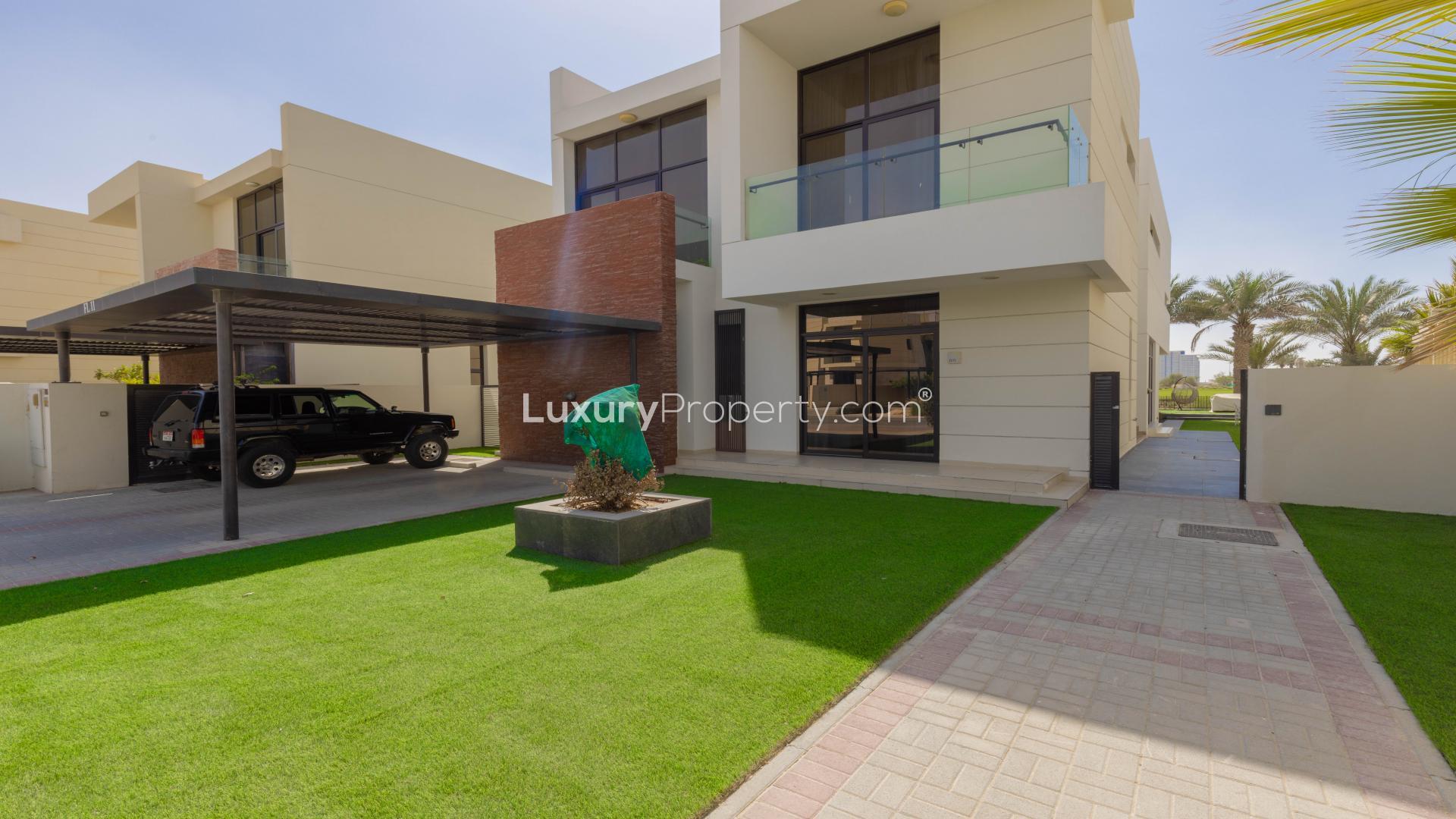"Balcony view of golf course at luxury Damac Hills villa in Flora community.","Modern villa exterior with landscaped garden, carport, and entrance in Damac Hills, Flora community.",Luxurious living room in Damac Hills villa with golf course views and elegant decor