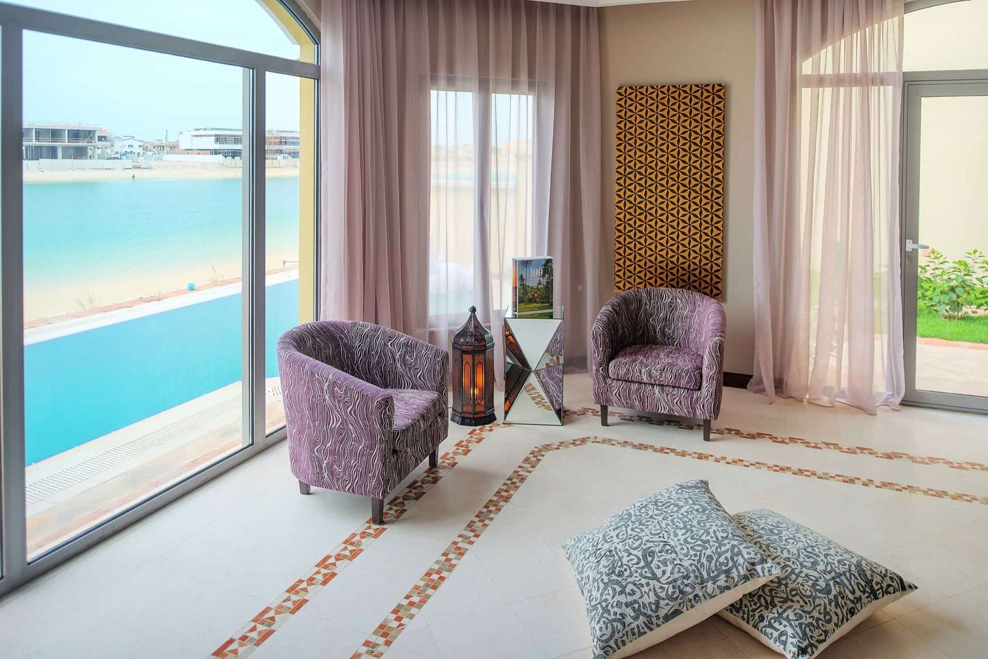"Stunning 6-bedroom villa exterior with lush garden on Palm Jumeirah, Dubai.",Luxurious living room in Palm Jumeirah villa with sea view and elegant decor