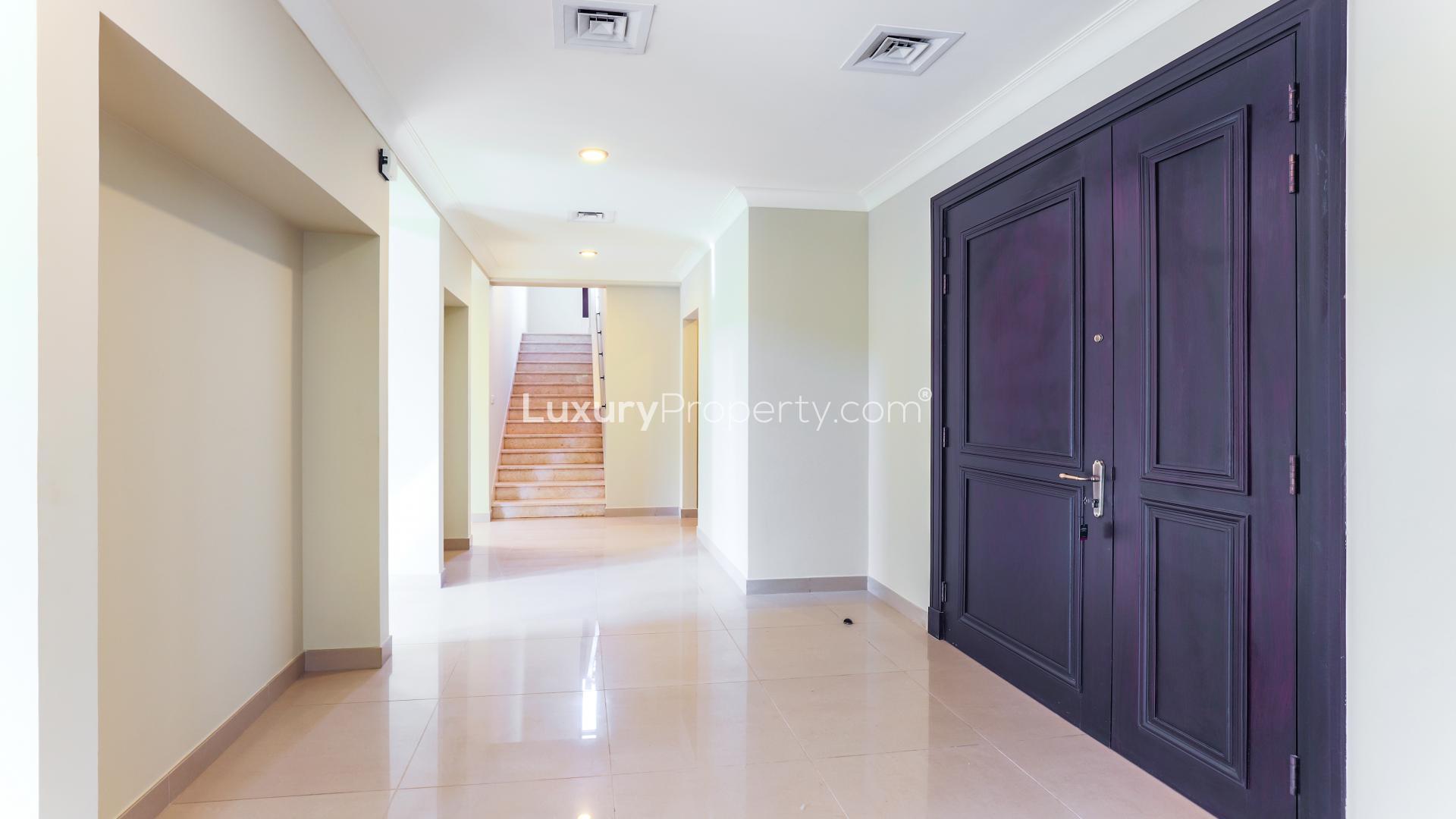 "Spacious villa patio with lush garden in Arabian Ranches 2, Rosa community for sale.",Luxurious entrance hallway in Arabian Ranches 2 villa, featuring elegant staircase and grand door