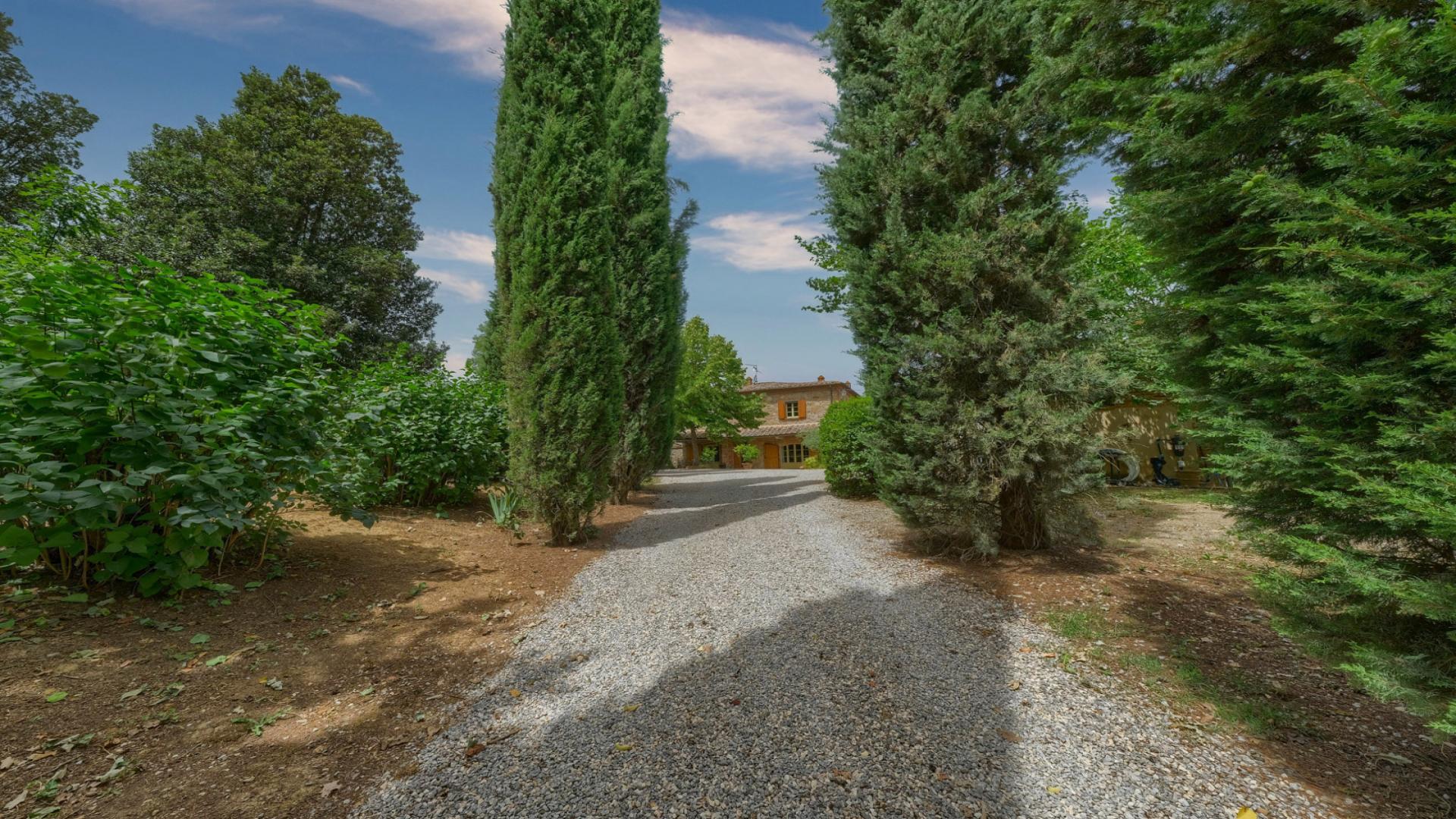 Charming stone villa exterior in Arezzo, surrounded by lush greenery and gravel driveway