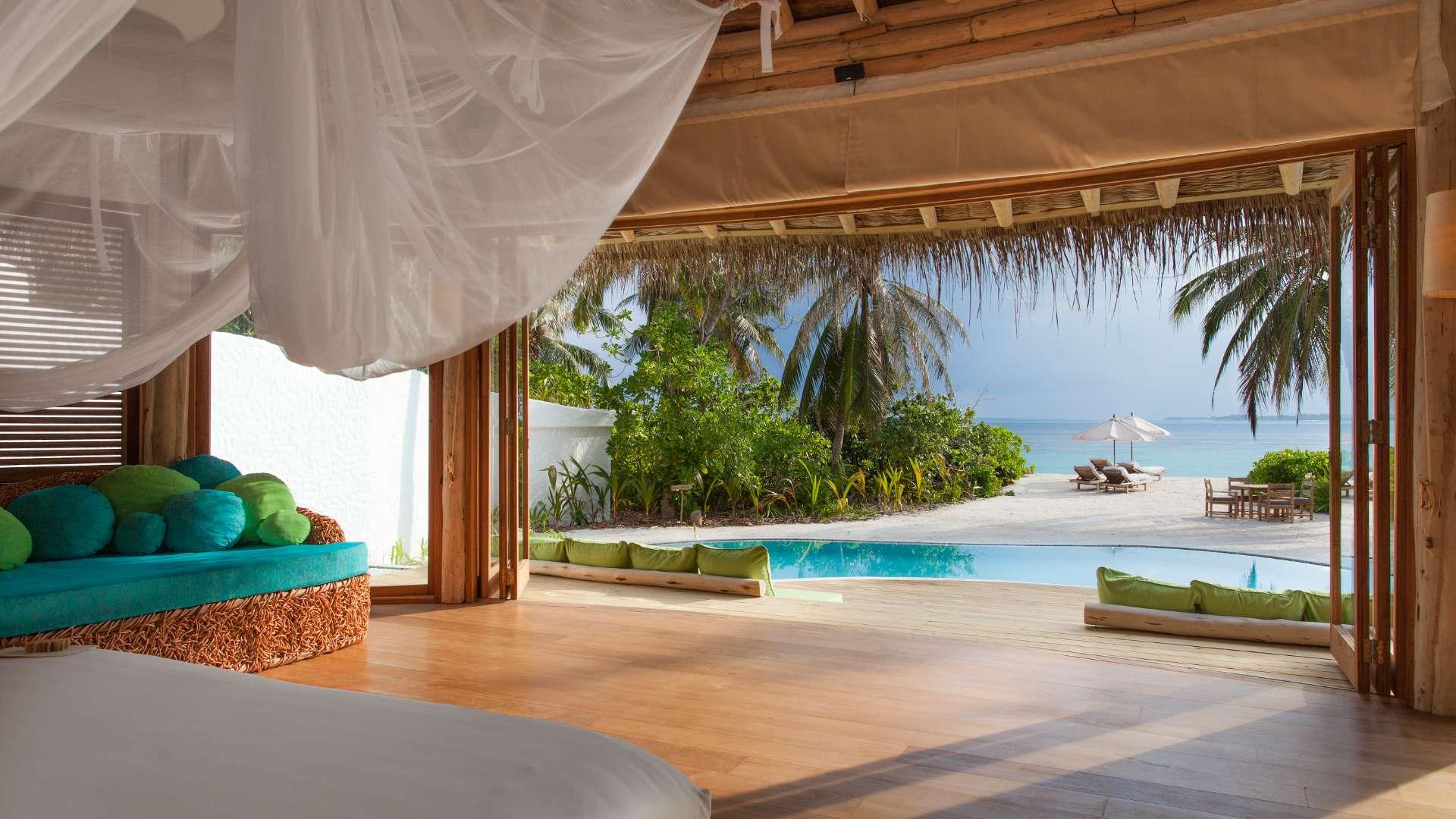 "Cozy living area in luxurious nine-bed villa, Soneva Fushi, Maldives, with rustic decor.",Luxurious Maldives villa bedroom with ocean view, pool, and beach access in Soneva Fushi