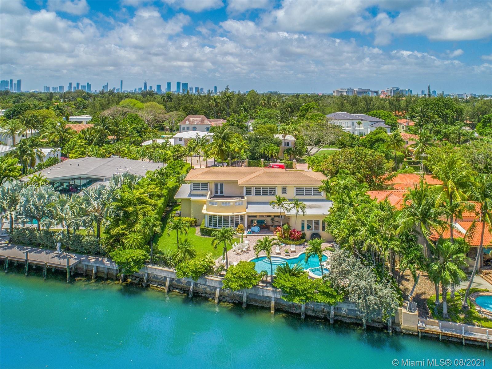 Aerial view of Miami Beach villa with canal, pool, lush greenery, and city skyline