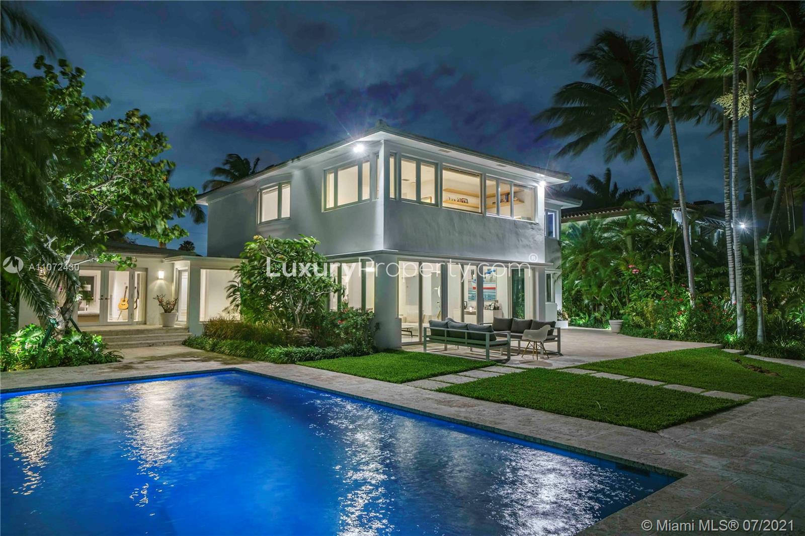 Luxury Miami villa exterior with lush garden and pool, evening view