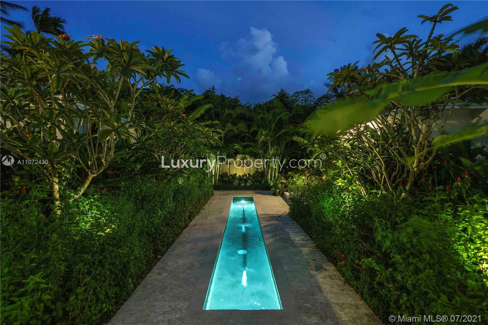 Luxury six-bedroom Miami villa with illuminated pool and lush garden at night