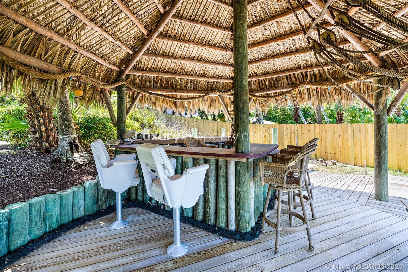"Waterfront view from luxury villa in Tequesta, Florida with private dock and sandy beach.",Tropical tiki bar with seating in luxury villa, Tequesta, Florida