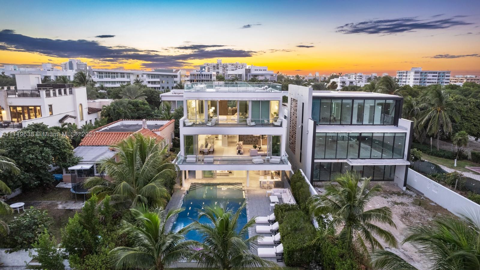 Oceanfront Miami villa with illuminated pool, modern design, and lush landscaping at night