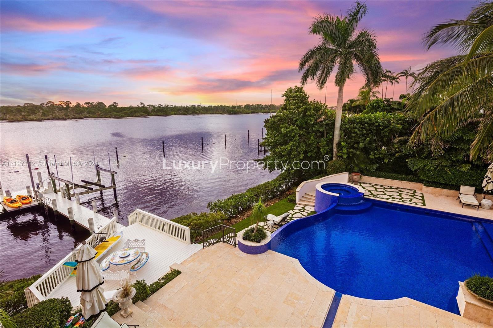 Luxurious waterfront villa patio with ornate furniture, palm trees, and serene river view