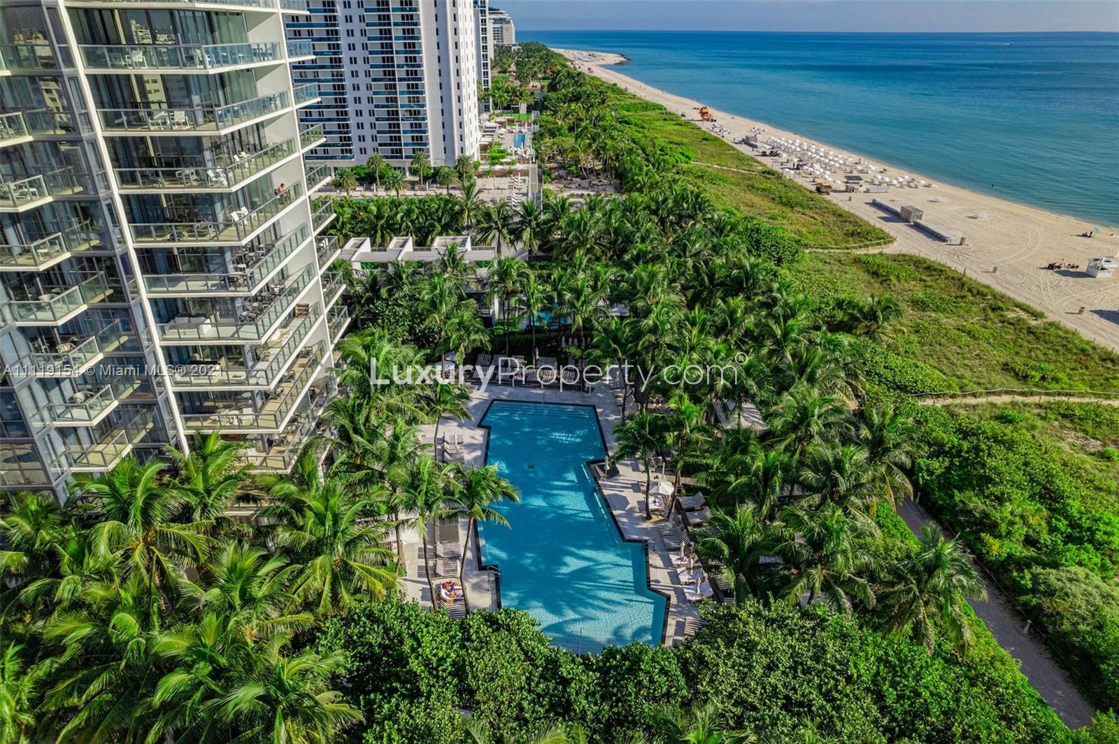 Oceanfront Miami beach view with pink loungers and umbrella near luxury penthouse for sale