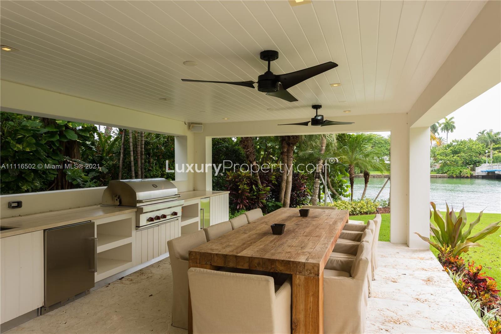 "Waterfront view from Miami villa dock, lush greenery, tranquil waters, LP10126 for sale.",Covered outdoor kitchen and dining area overlooking waterfront at Miami villa, Florida