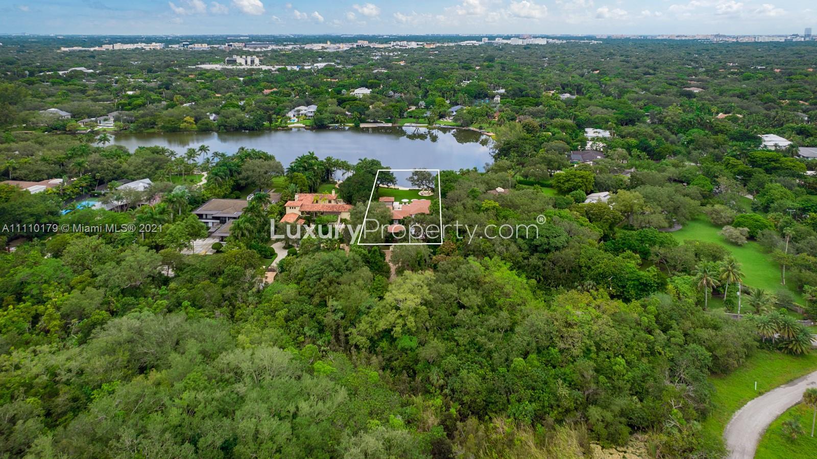 Luxurious Miami villa entrance with lush greenery and elegant gated driveway for sale