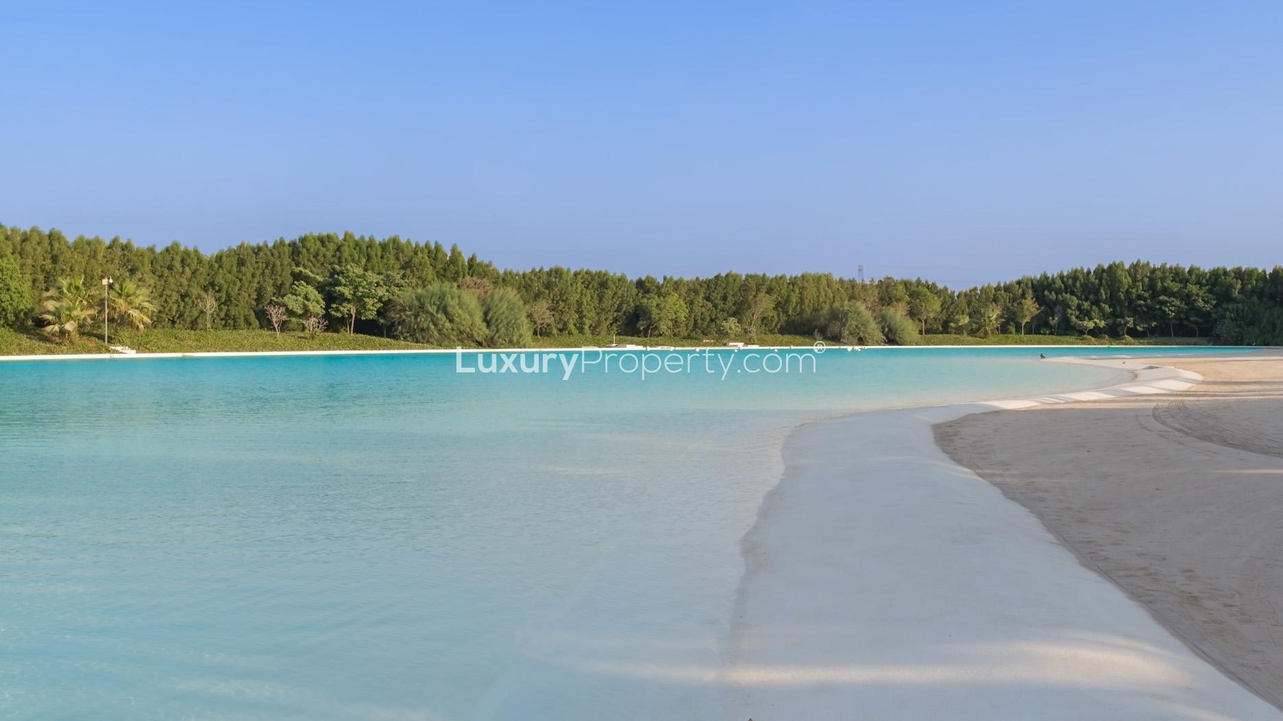 Alt text: "Stunning waterfront view of District One, MBR City skyline with lush greenery.",Triple-sized plot with stunning beachfront in MBR City, District One, for sale.