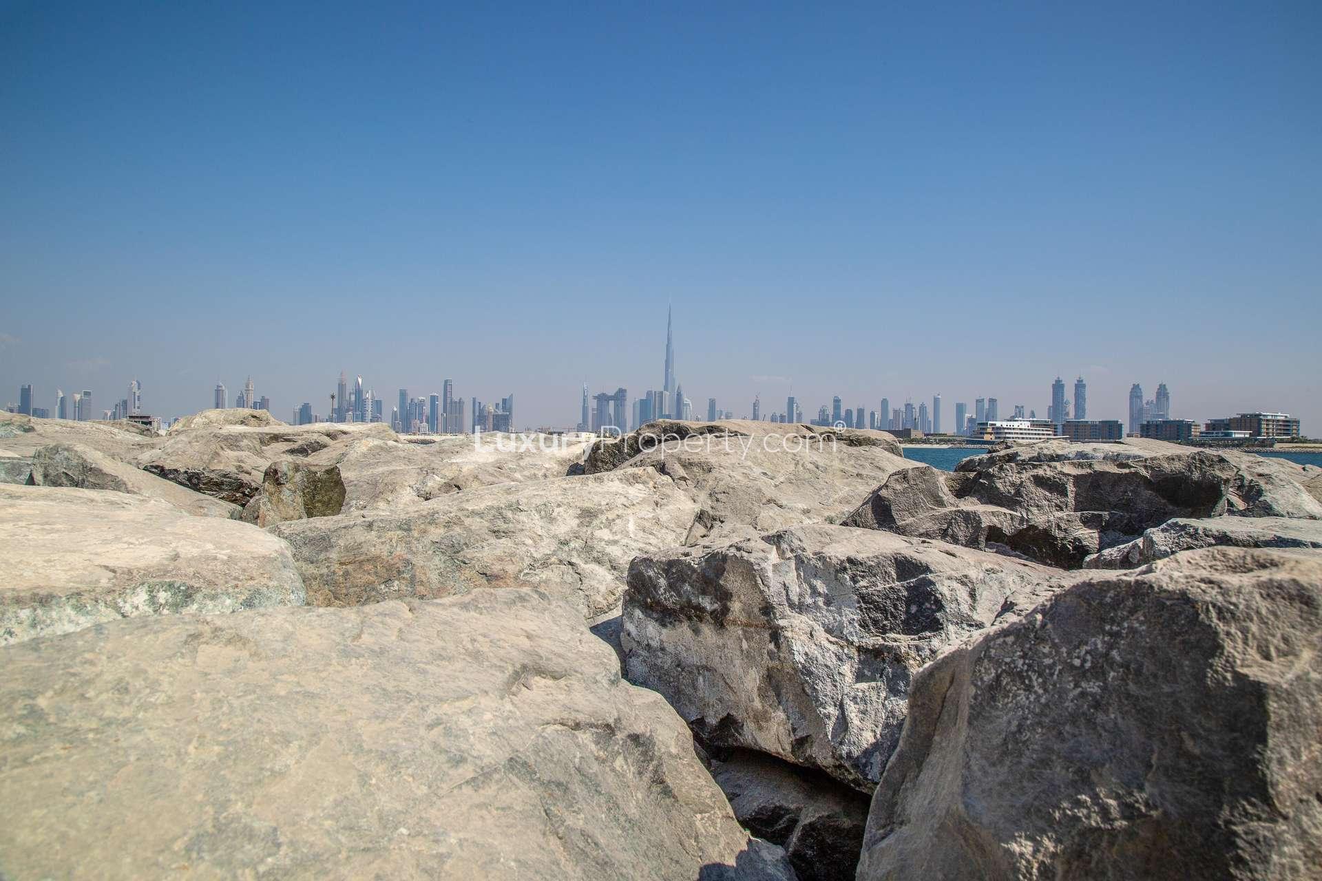 "Stunning Dubai skyline view from Jumeirah Bay Island, perfect for luxury island living.",Rocky shoreline with Dubai skyline view from Jumeirah Bay Island, perfect for luxury living