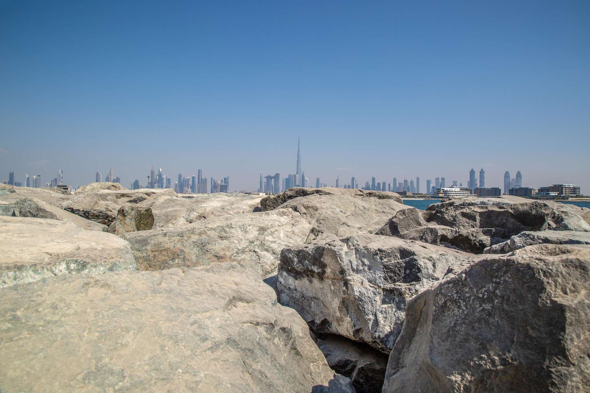 "Stunning Dubai skyline view from Jumeirah Bay Island, perfect for luxury island living.",Rocky shoreline with Dubai skyline view from Jumeirah Bay Island, perfect for luxury living